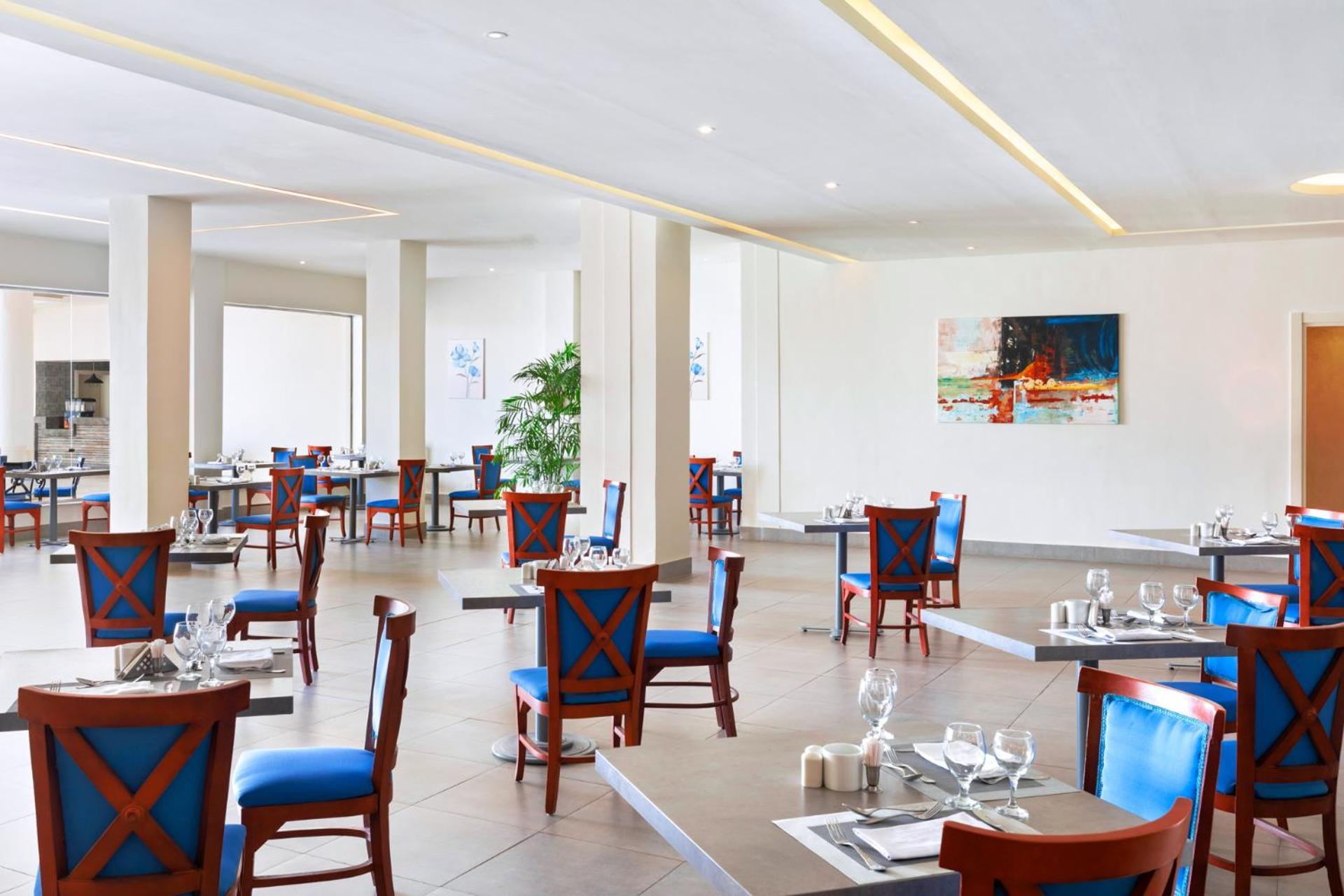 Pickalbatros Royal Grand Sharm - Adults Friendly 16 Years Plus Εξωτερικό φωτογραφία The photo shows an interior of a restaurant featuring a modern and spacious design. The floors are tiled, and the walls are painted in neutral tones. The seating consists of wooden chairs with blue cushions arranged around tables, which are set with 