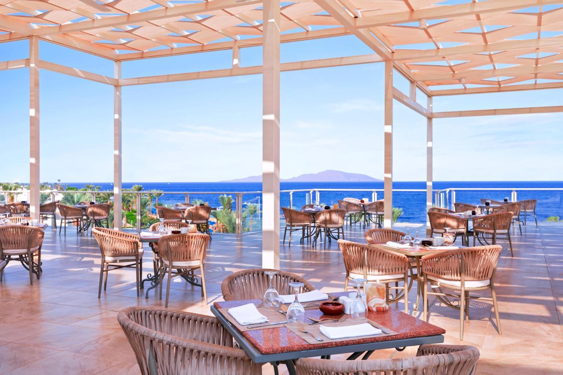 Pickalbatros Royal Grand Sharm - Adults Friendly 16 Years Plus Εξωτερικό φωτογραφία The photo shows a spacious outdoor restaurant with a beautiful view of the ocean. The seating area features several tables and wicker chairs. The open design includes a wooden pergola providing some shade, while large windows or openings allow for a 