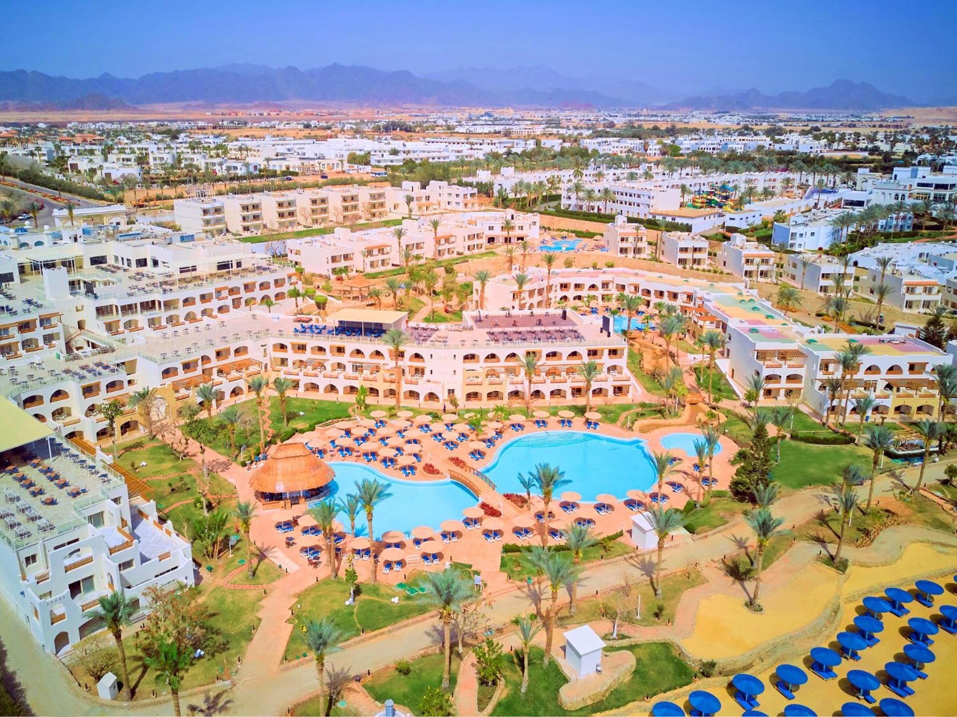 Pickalbatros Royal Grand Sharm - Adults Friendly 16 Years Plus Εξωτερικό φωτογραφία The photo shows an aerial view of a resort complex. There are several buildings arranged around a central area that features swimming pools. The pools are surrounded by palm trees and lounge chairs, indicating a tropical or sunny climate. In the back