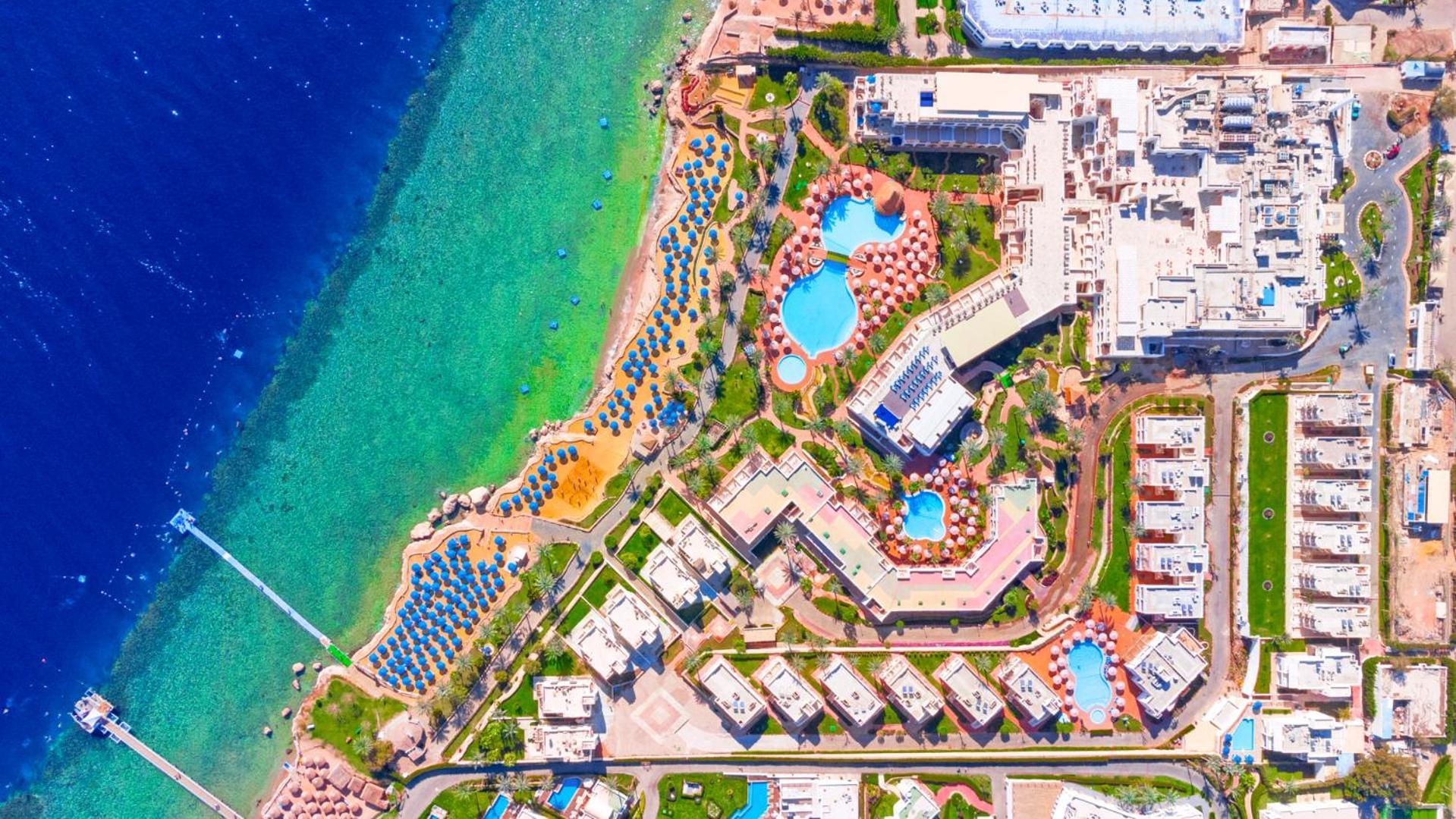 Pickalbatros Royal Grand Sharm - Adults Friendly 16 Years Plus Εξωτερικό φωτογραφία The image shows an aerial view of a coastal resort area. It features various swimming pools outlined by landscaped gardens and pathways. There are also rows of sun loungers and umbrellas near the beach. The water transitions from a deep blue to a vib