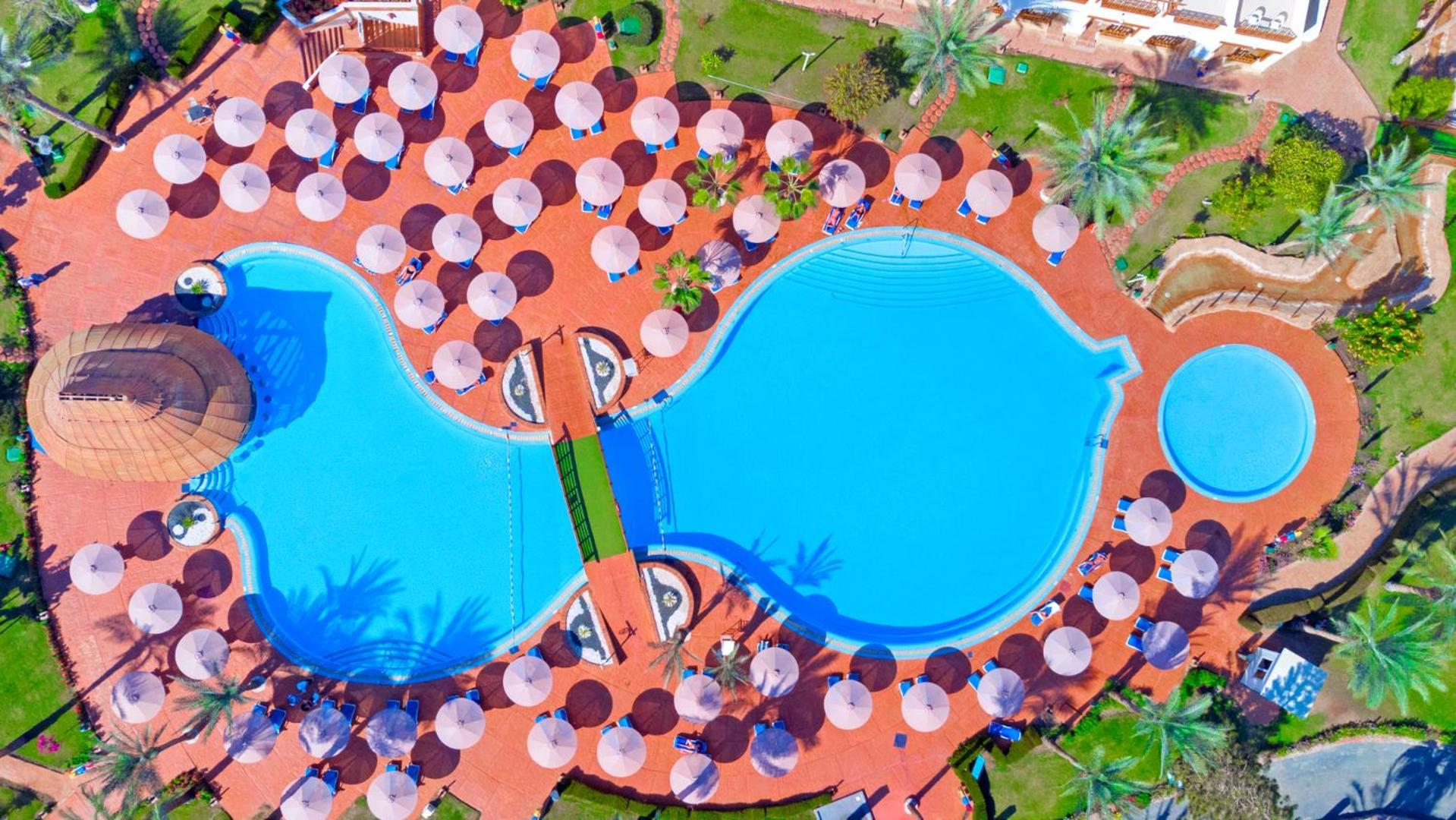 Pickalbatros Royal Grand Sharm - Adults Friendly 16 Years Plus Εξωτερικό φωτογραφία The photo shows an aerial view of a large swimming pool area, shaped in a distinctive layout resembling two interconnected pools. Surrounding the main pool are numerous umbrellas, providing shade for visitors. The pool area is set on a reddish-colore