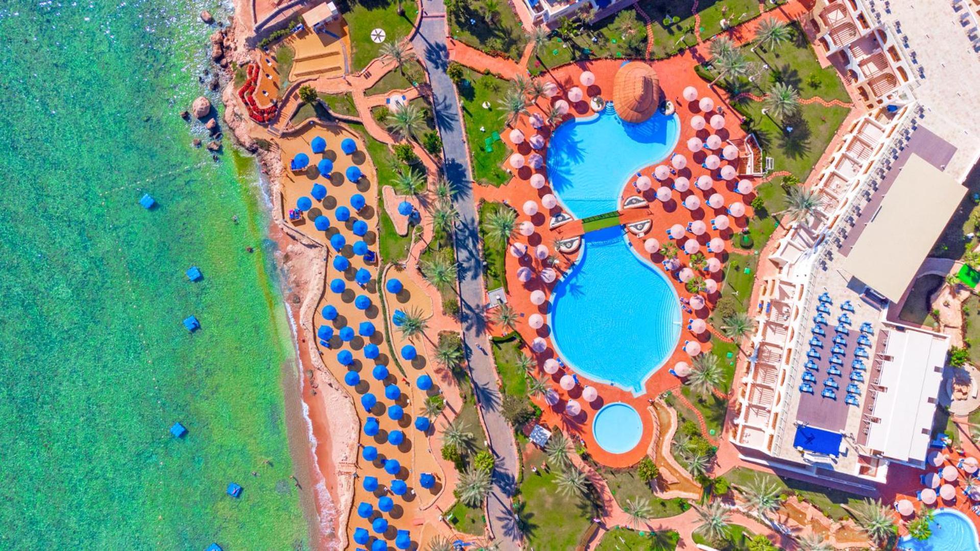Pickalbatros Royal Grand Sharm - Adults Friendly 16 Years Plus Εξωτερικό φωτογραφία The photo shows an aerial view of a beach resort. In the foreground, there's a large swimming pool shaped like a flowing river, surrounded by lounge chairs and umbrellas. The pool has a distinctive, organic design with curved edges. To the left, ther