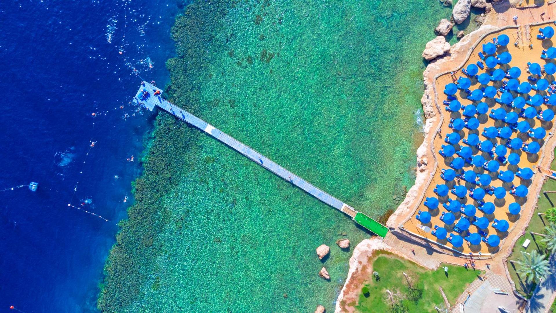 Pickalbatros Royal Grand Sharm - Adults Friendly 16 Years Plus Εξωτερικό φωτογραφία The photo shows an aerial view of a coastal area featuring a long wooden pier extending into clear turquoise water. On one side of the pier, there appears to be a beach with umbrellas or sunbeds arranged neatly. The water is vibrant and visually invi