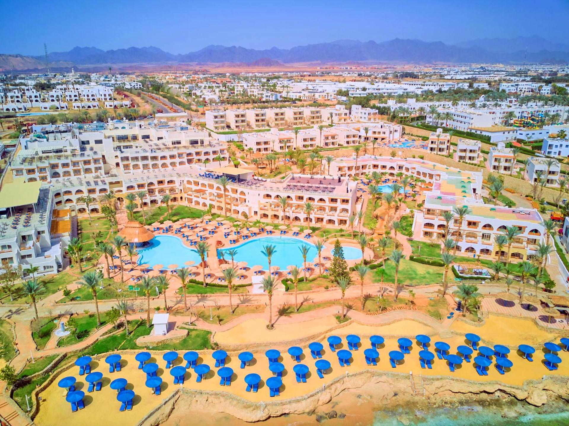 Pickalbatros Royal Grand Sharm - Adults Friendly 16 Years Plus Εξωτερικό φωτογραφία The photo shows a large resort complex set in a scenic location, likely near a beach. The layout features multiple buildings with a Mediterranean style of architecture, surrounded by lush greenery and palm trees. Central to the resort is a swimming p