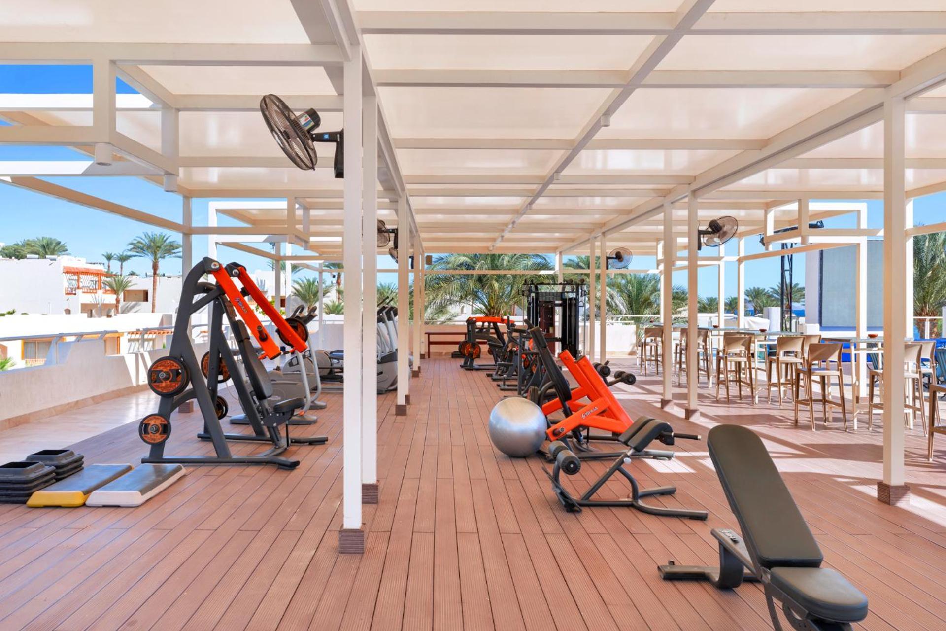 Pickalbatros Royal Grand Sharm - Adults Friendly 16 Years Plus Εξωτερικό φωτογραφία The photo depicts a gym area located outdoors or in a covered terrace, featuring various fitness equipment. There are several weight machines and benches, as well as some free weights. Large fans are installed for ventilation, and the space is design