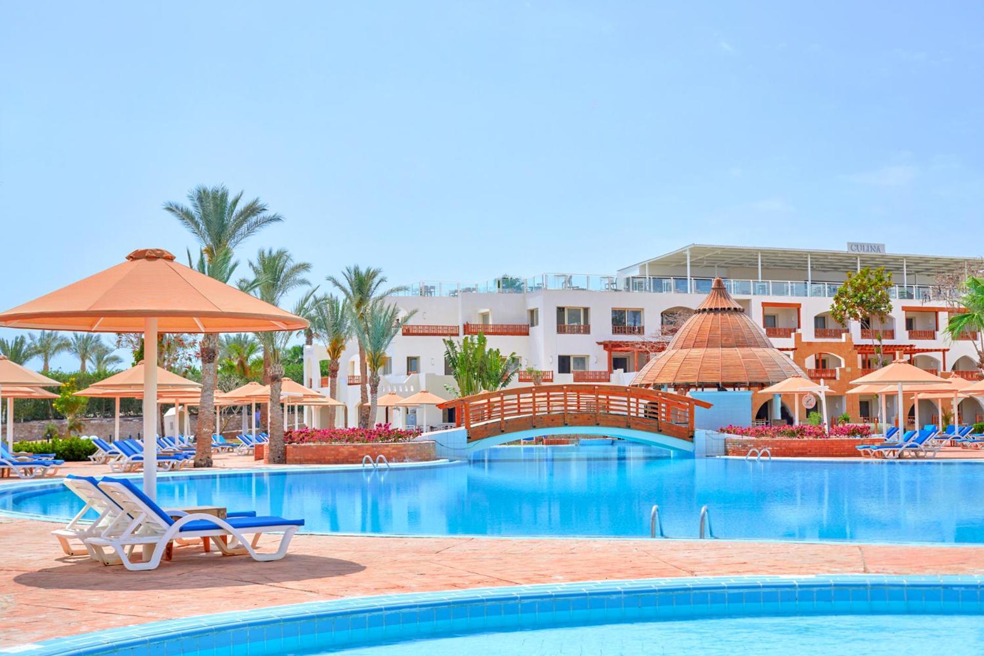 Pickalbatros Royal Grand Sharm - Adults Friendly 16 Years Plus Εξωτερικό φωτογραφία The photo depicts a beautiful resort setting featuring a large, inviting swimming pool. There are several lounge chairs positioned around the pool, along with straw umbrellas providing shade. In the background, there is a charming wooden bridge archi
