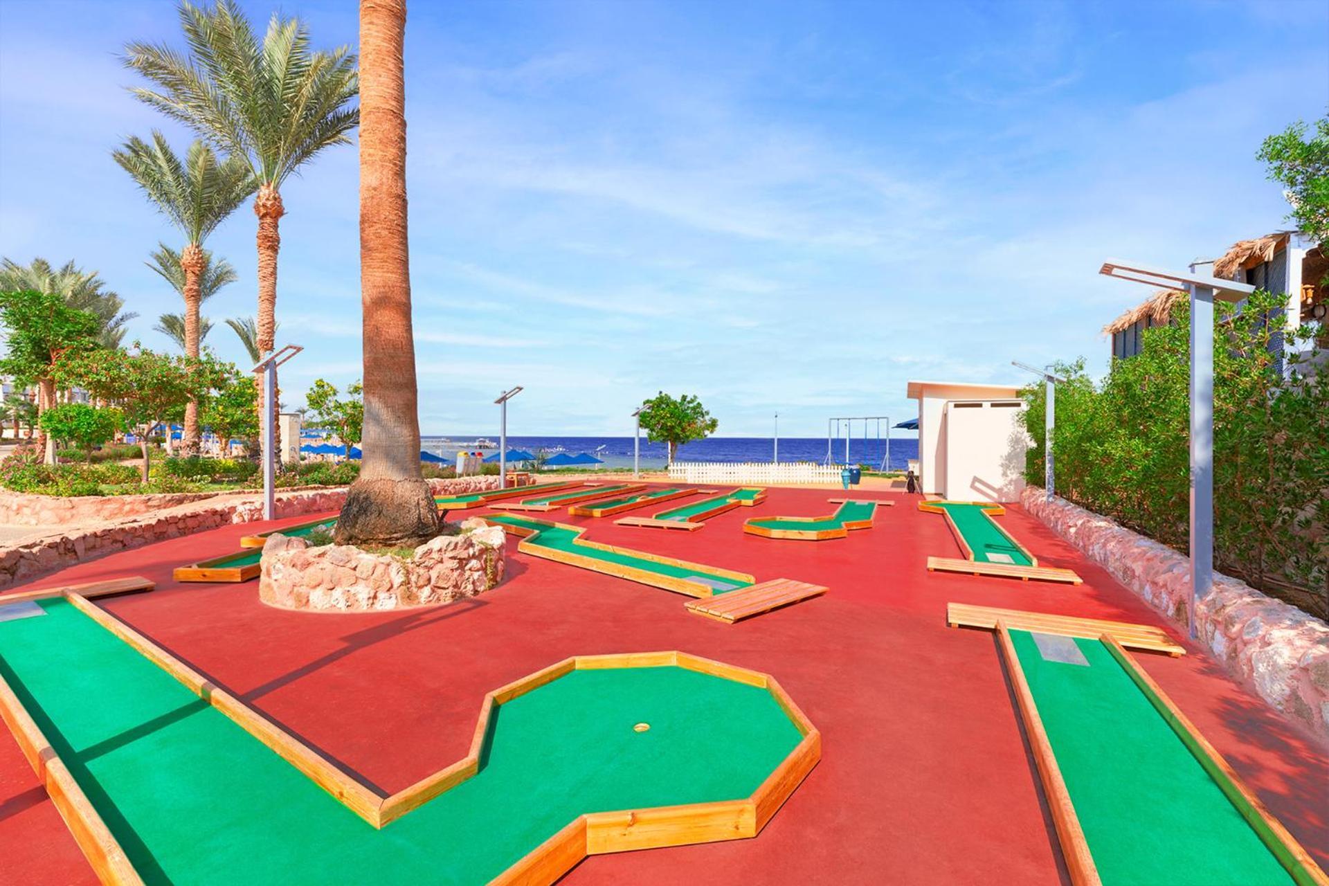 Pickalbatros Royal Grand Sharm - Adults Friendly 16 Years Plus Εξωτερικό φωτογραφία The photo shows a mini-golf course situated outdoors, with a view of the sea in the background. The course features vibrant green and red surfaces, laid out in winding patterns, and surrounded by well-maintained landscaping, including palm trees. The